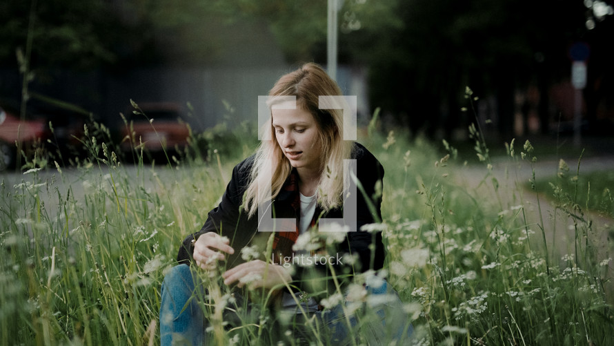 a young woman sitting in tall grass outdoors 