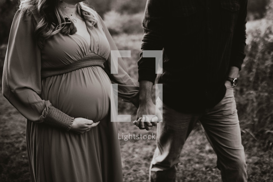 a pregnant woman and her husband hold hands