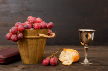 Cup with wine, bread, grapes and bible on wodd table