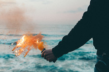 a man holding a flare standing by the ocean 