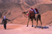 A man leading a camel through the desert 