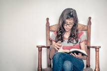 girl child sitting in a chair reading a Bible 