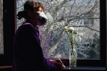 woman looking out a window wearing a mask 
