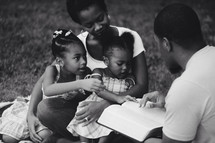 Family reading the Bible together outside.