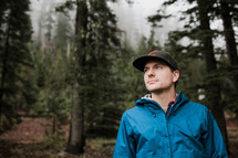 a man in a raincoat standing in a forest alone 