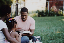 Family reading the Bible together outdoors.