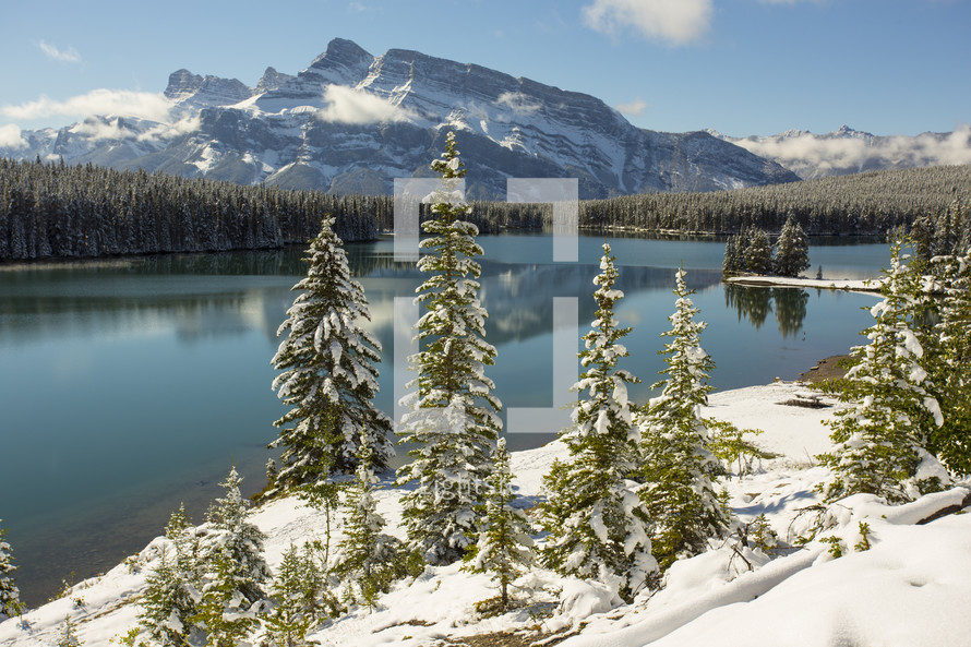 A placid lake surrounded by snow covered trees and mountains.