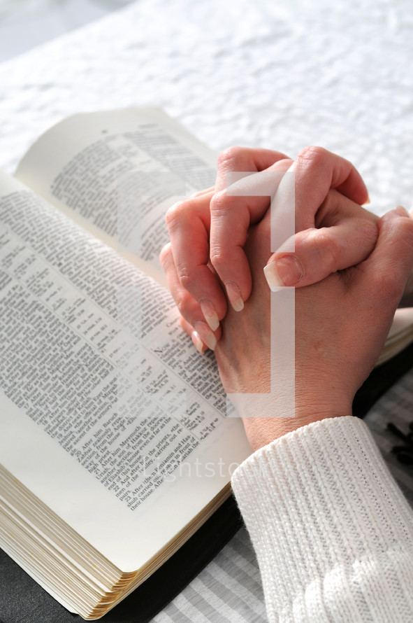 Hands folded resting on a bible