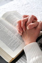 Hands folded resting on a bible
