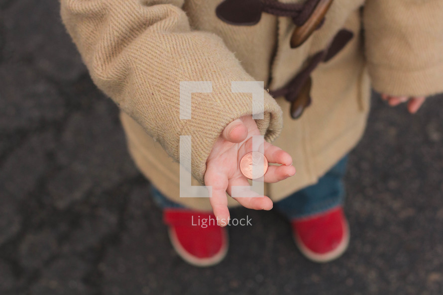 Child standing outside holding a penny.