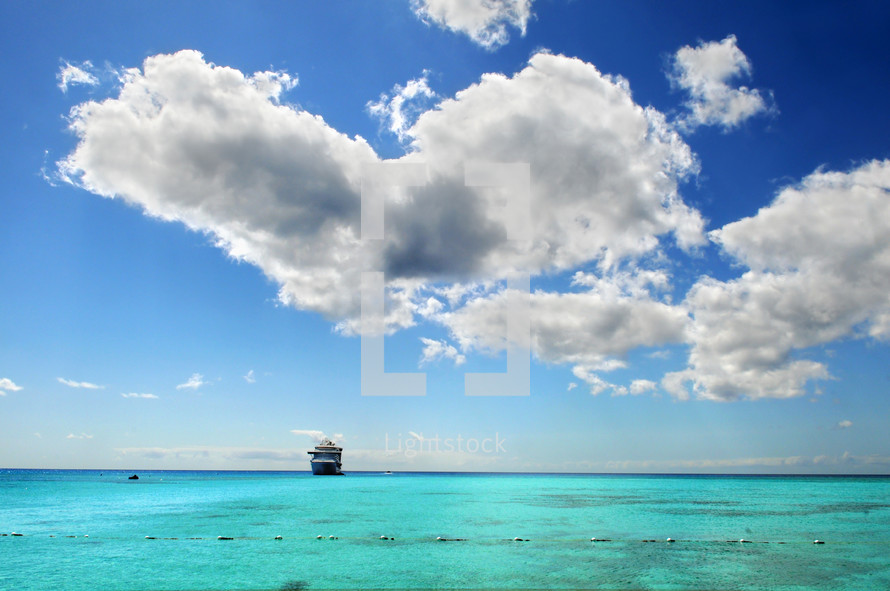 View of ocean, a ship in the distance , blue sky with white clouds