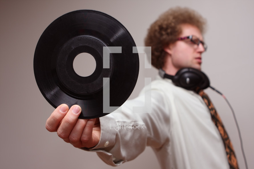 A man wearing headphones and holding out a vinyl record.