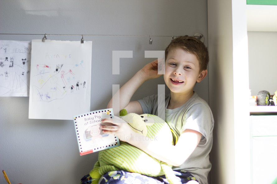 young boy holding a stuff animal, showing off his art work