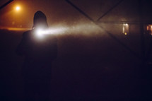 A man holding a flashlight in the foggy night