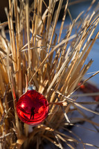 red Christmas ornament on dry grasses outdoors 