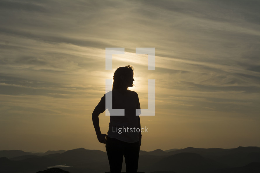 silhouette of a woman standing on a mountaintop at sunset 
