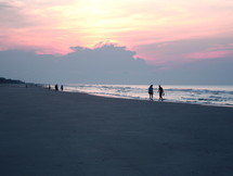 Silhouettes of people walking along the beach at sunrise.