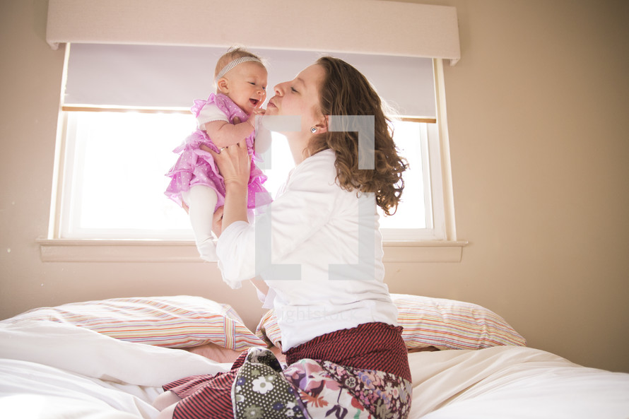 a mother on a bed kissing her infant daughter 