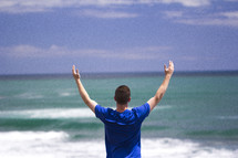 man with raised hands standing on a beach 