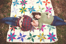 Couple laying on a quilt in the grass.
