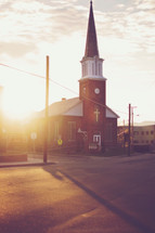 Sun shining behind a church with a tall steeple.