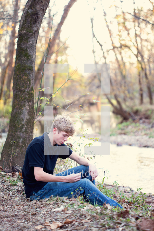 young man sitting by the edge of a creek 