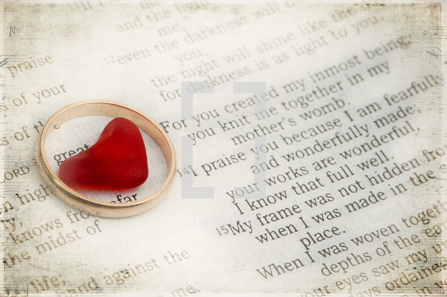 Heart in a gold wedding band on top of a Bible open to Psalm 139.