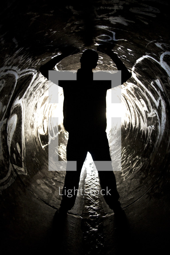 Man straddling water flowing through a sewer drain pipe with arms raised.