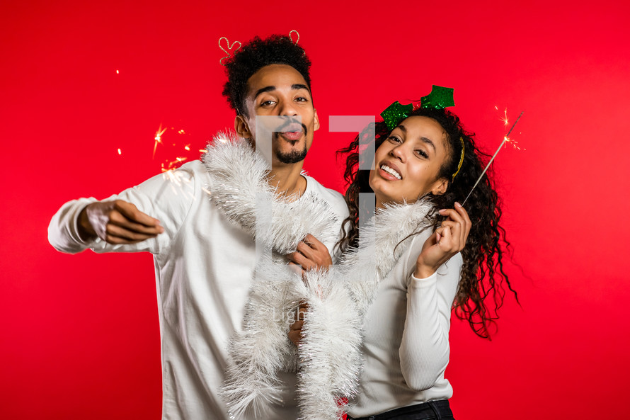 Young african american couple with christmas bengal fire sparklers isolated on red background studio. New 2025 year decorations, party, happiness concept. High quality photo

