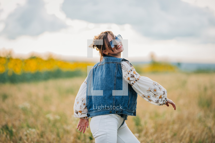 Smiling attractive hippy woman on nature background. Young lady in white embroidery shirt, denim waistcoat. Summer fashion, hipster, ethno, folk lifestyle.