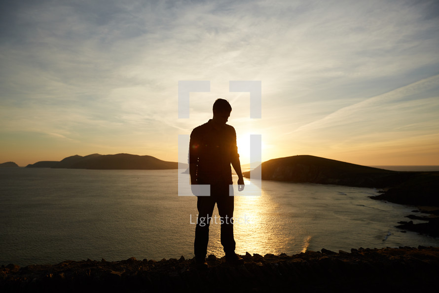 silhouette of a man standing by a shore at sunset 