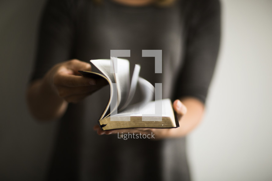 A woman opening a Bible and flipping through the pages. 
