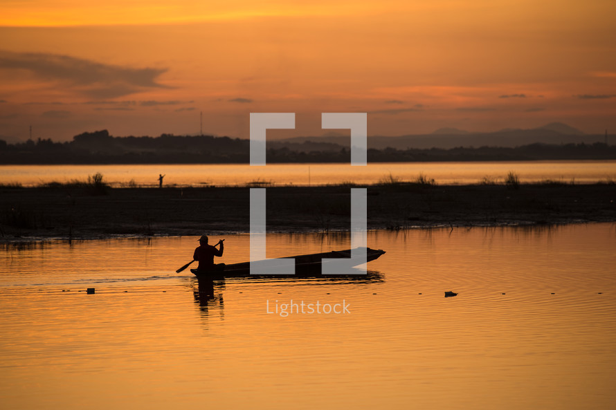 Silhouette of a man with an oar in a boat on the lake water at sunset.