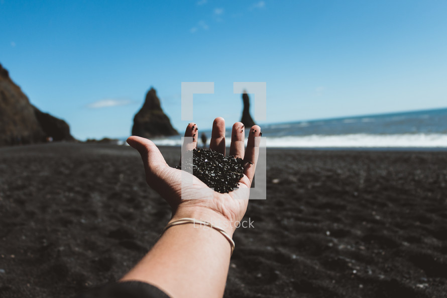 a person holding black sand standing on a beach 