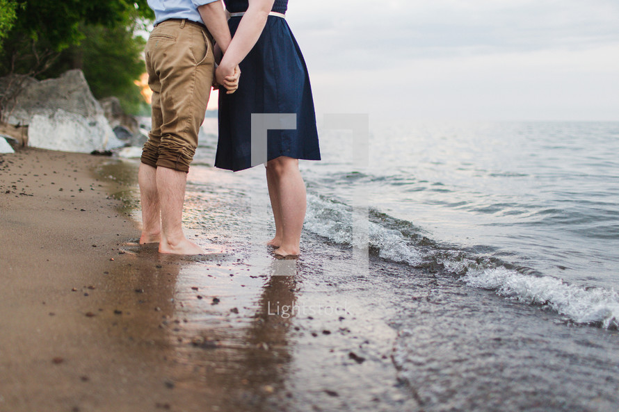 a couple holding hands standing on a beach 