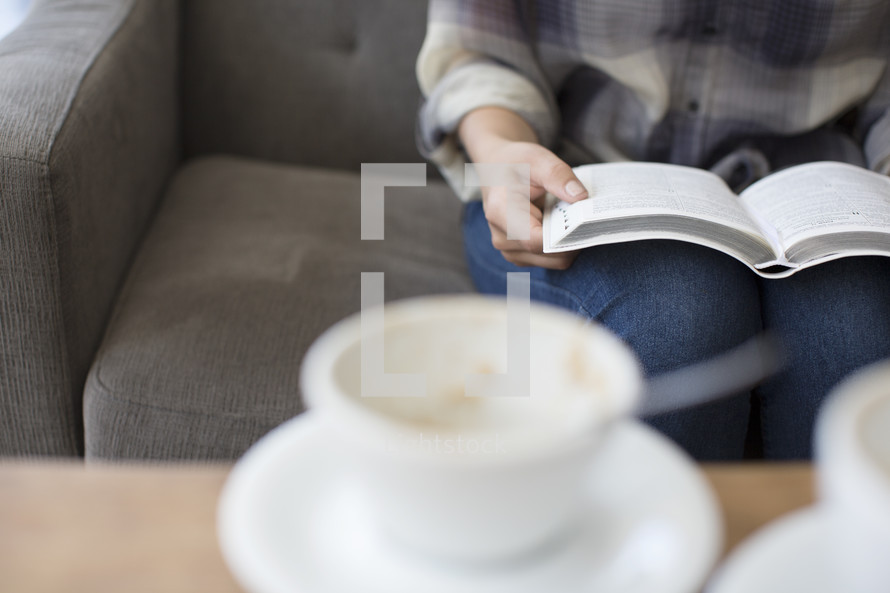 woman sitting on a couch reading and a coffee cup 