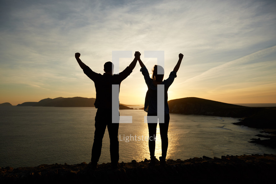 a couple holding raised hands at sunset 