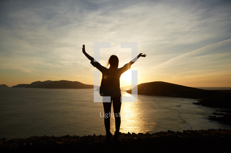 a woman with raised hands at sunset 