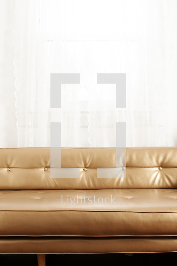 gold leather couch in front of a window.