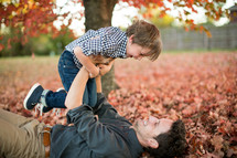 a father and son playing in fall leaves 