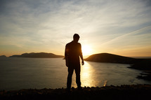 silhouette of a man standing by a shore at sunset 