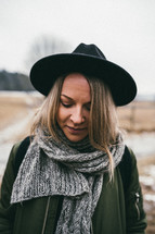 a woman in a hat, coat, and scarf looking down