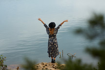 woman in a dress standing on a shore  with hands raised 