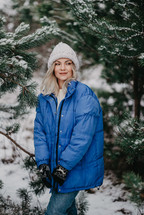 Portrait of young pretty woman in forest, winter season. Attractive kind blonde girl smiling, lady in white knitted hat. High quality