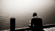 A man reading his Bible on the edge of a dock