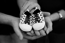 open hands of a mother and father holding empty baby shoes