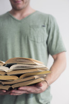 man holding open books stacked in a pile
