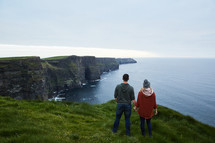 a couple standing at the edge of a cliff holding hands 