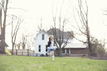 A little girl runs across the yard behind her house.