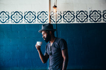 African American man holding a coffee cup standing in front of a blue wall 